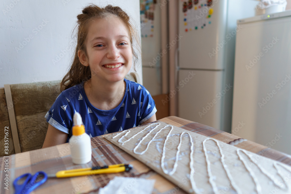 the girl makes crafts, glues cardboard, sits in the home kitchen the girl makes crafts, glues cardboard, sits in the home kitchen