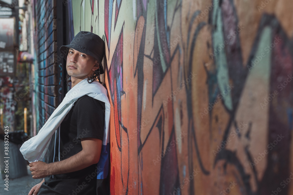 Mexican Latin young man leaning on the wall, urban portrait wearing black hat