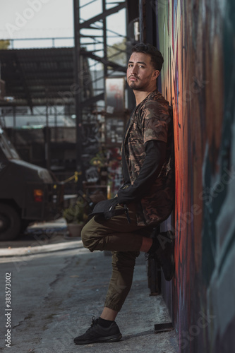 Mexican Latin young man leaning on the wall, urban portrait wearing military clothing