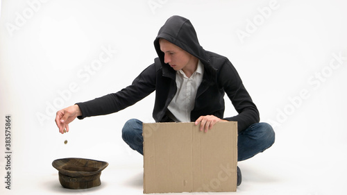 Young begging man dumps donation into his hat. Blank cardboard sign for copyspace. photo