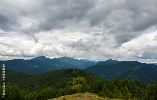 A scenic view of the mountains landscape, forest, meadows and pasture on the background with a cloudy sky covering the Carpathian ridge, Ukraine