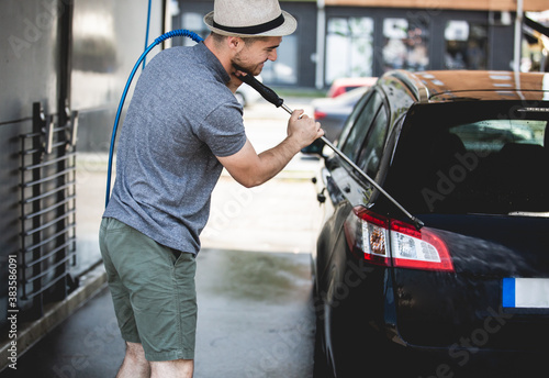 Young man cleaning automobile with high pressure water jet at car wash.