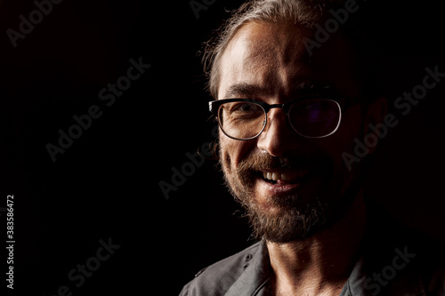 Dark studio portrait of a middle-aged man with beard in glasses