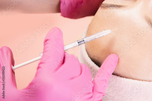 Woman getting injection procedure for tightening and smoothing wrinkles on forehead face skin. Beauty salon care, pink color