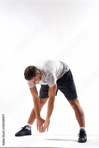 A sports man in shorts and a full-length T-shirt does exercises on a light background