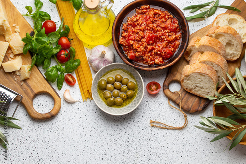 Tomato Bolognese sauce, spaghetti, cheese parmesan, olives, ciabatta, snacks on white rustic background. Ingredients for cooking Italian pasta or mediterranean healthy dinner, top view, copy space