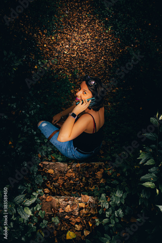 Fototapeta Naklejka Na Ścianę i Meble -  beautiful girl sitting on a staircase in the middle of the forest talking on the phone with her friends. travel and adventure