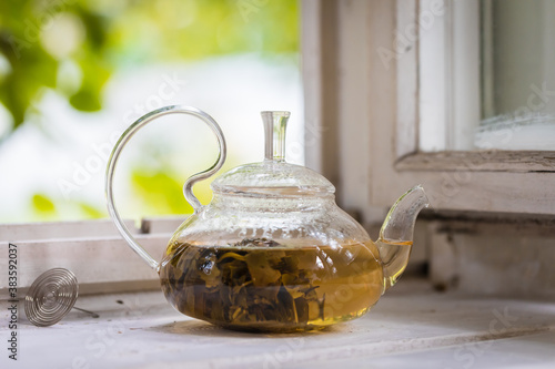 Green tea in a glass teapot on rustic background, selective focus
