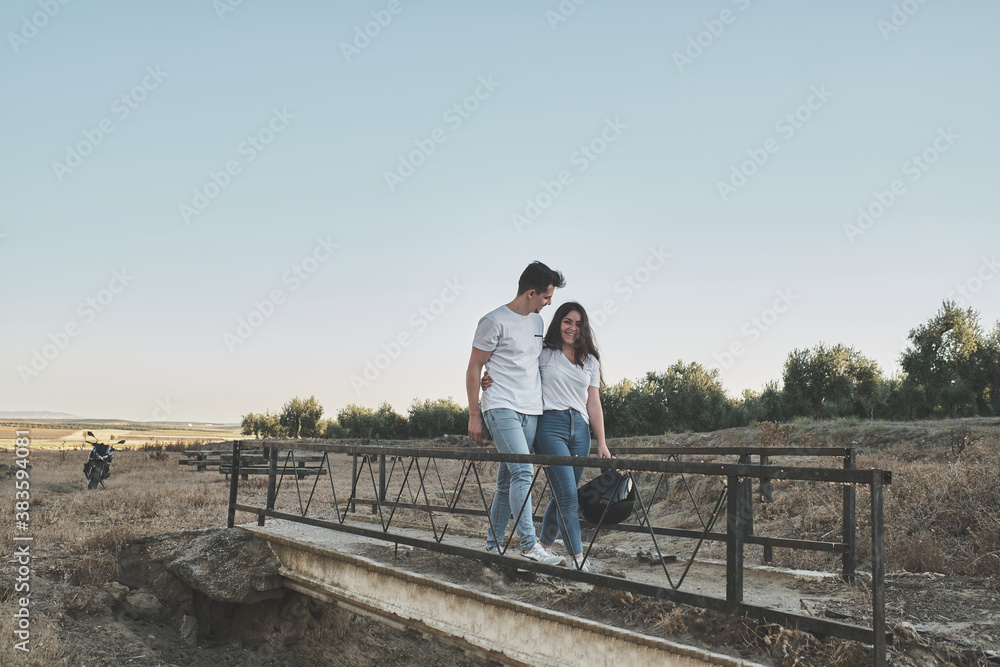 couple walking on an old bridge with their motorcycle parked behind couple walking on an old bridge with their motorcycle parked behind