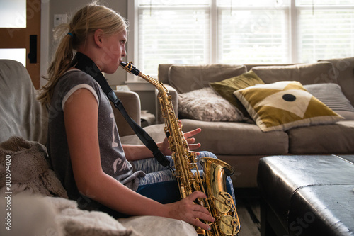 Young girl with blonde ponytail playing the alto saxophone in a living room