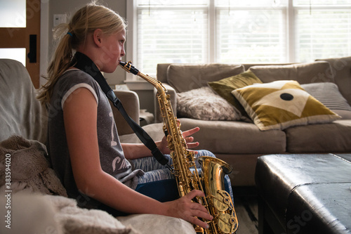Young girl with blonde ponytail playing the alto saxophone in a living room photo