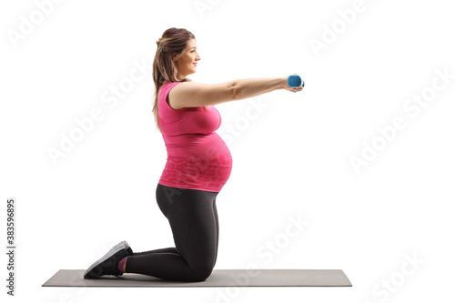 Fototapeta Naklejka Na Ścianę i Meble -  Full length profile shot of a pregnant woman kneeling on a mat and exercising with dumbbells