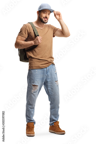 Full length portrait of a young man with a backpack and ripped jeans holding his cap