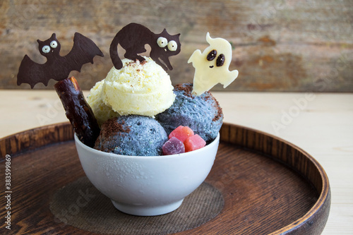 Halloween dessert in a white cup. It consists of ice cream and chocolate black cat, bat and ghost. Creative food for the holiday and good mood.