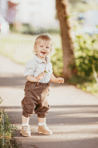A small blond boy dressed in a vintage jumpsuit in a field at sunset