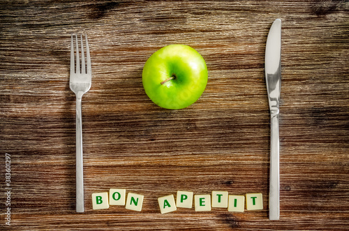 Slika na platnu Silverware and apple on wooden table with Bon apetit sign
