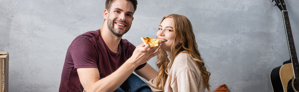 panoramic concept of pleased man feeding girlfriend with pizza