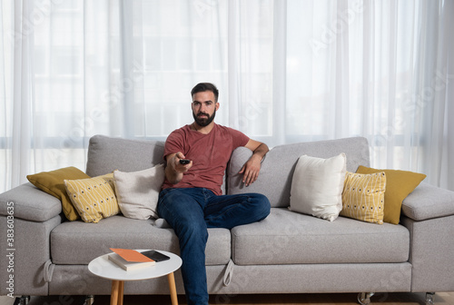Young casual man sitting on the sofa at his home with remote control in his hand relaxing with television program © Srdjan