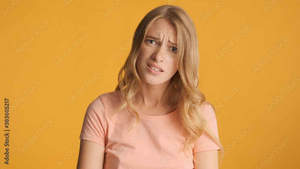 Sad girl with frowning face posing on camera over yellow backgro Sad girl with frowning face posing on camera over yellow backgro