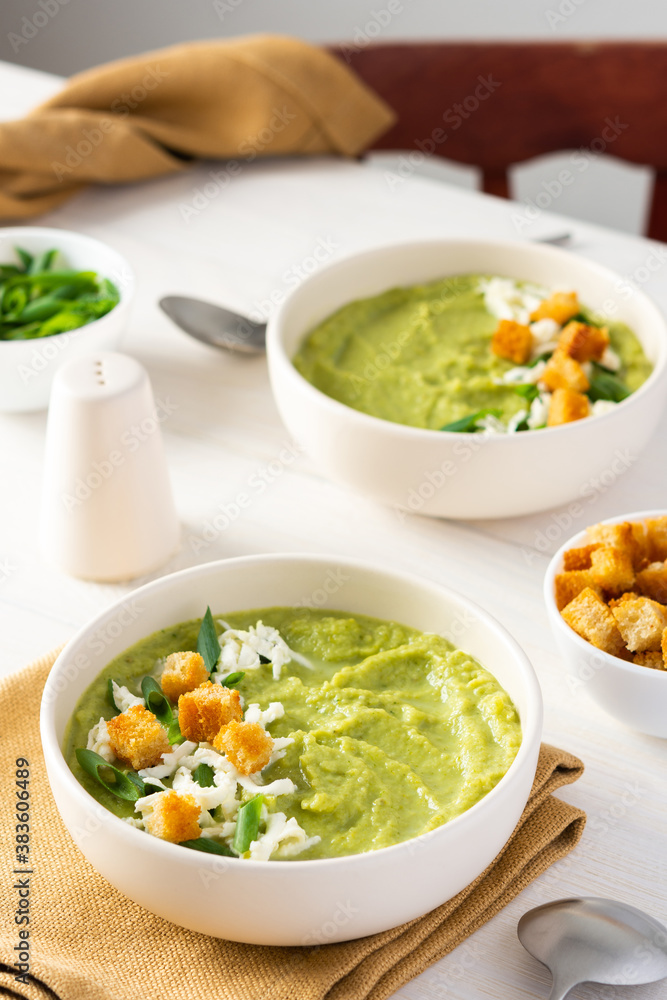 Healthy delicious broccoli and cucumber cream puree soup with mozzarella, green onions and croutons, bowl of soup on a white table Healthy delicious broccoli and cucumber cream puree soup with mozzarella, green onions and croutons, bowl of soup on a white table