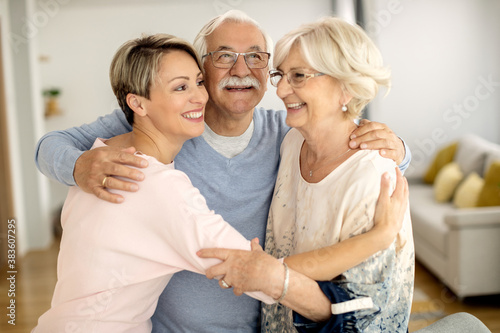Happy senior couple and their adult daughter embracing at home.