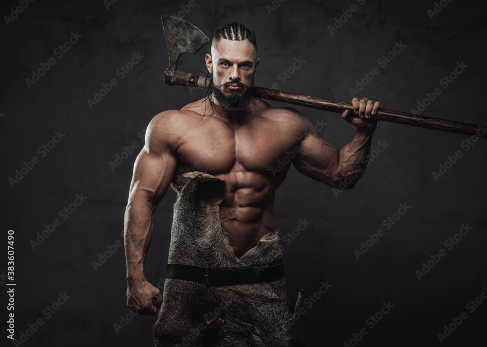 Obraz premium Powerful northen marauder with dreadlocks and black beard posing holding his axe behind shoulders in dark grunge background.