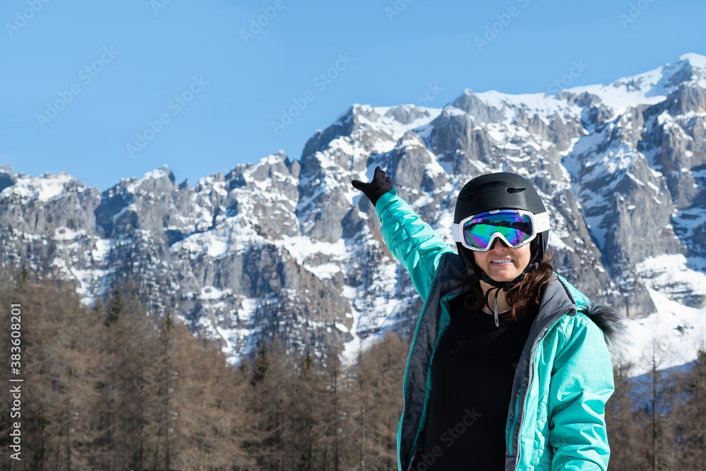 A woman in a colorful ski suit, helmet and sunglasses after skiing stands against the backdrop of mountain peaks. Sports concept, people, travel.