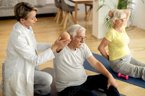 Physical therapist assisting mature couple with exercises at home.