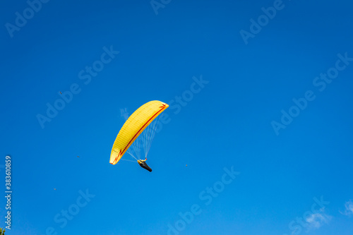 A paraglider with a bright yellow parachute against a clear blue sky