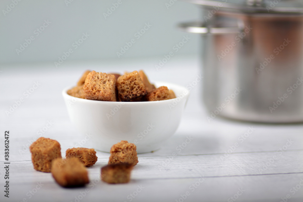 white bowl of croutons and saucepan of soup on white wooden background white bowl of croutons and saucepan of soup on white wooden background