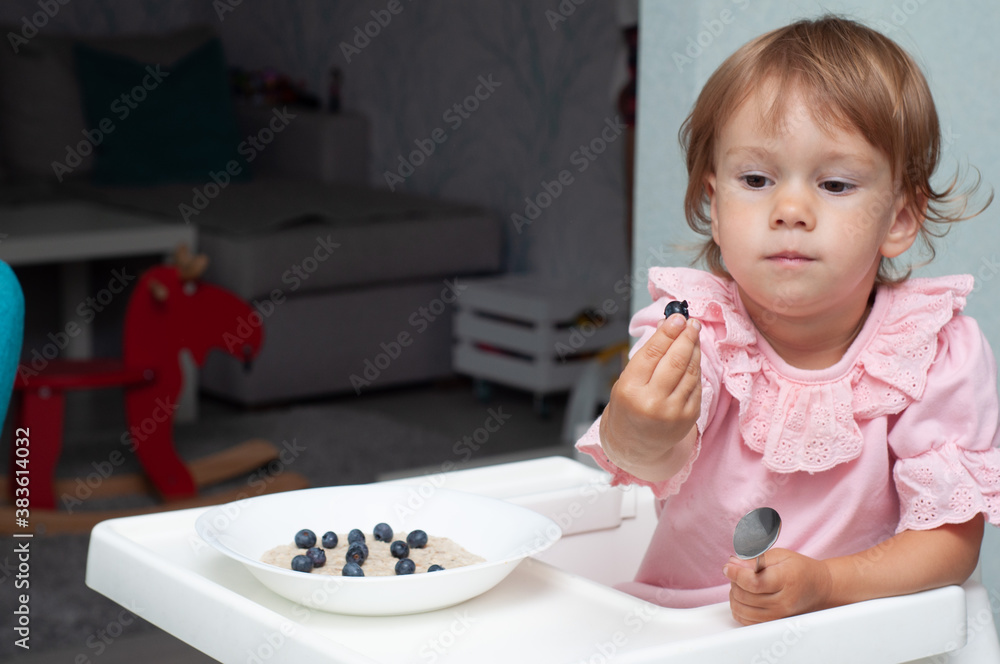 Happy, smiling child eating oatmeal with berries. The concept of a healthy breakfast for children, porridge with blueberries on baby chair Happy, smiling child eating oatmeal with berries. The concept of a healthy breakfast for children, porridge with blueberries on baby chair