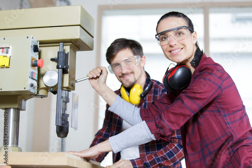 happy engineer instructing female apprentice on use of drill