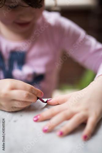 Young girl child entertaining herself painting her nails purple with nailpolish and a brush 