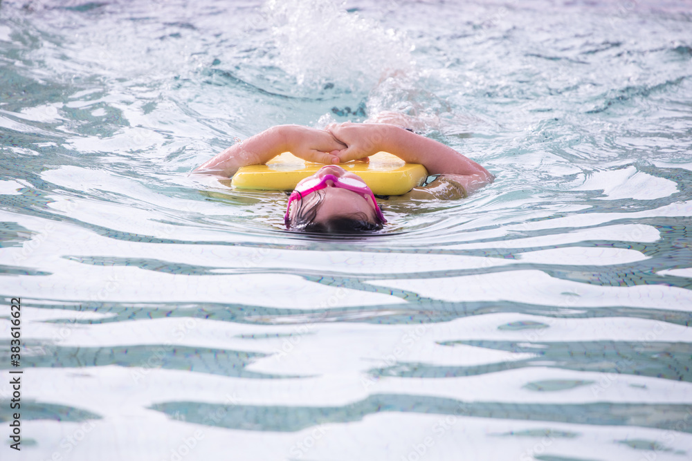 Fit and healthy you child trying to keep healthy learn to swim lesson outdoors in a salt water outdoor pool wearing pink goggles and holding yellow kick board splash 