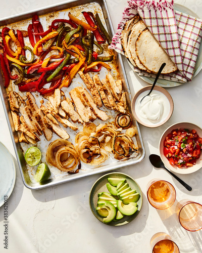 Overhead view of chicken fajitas with roasted vegetables in sheet pan and tacos served on table photo