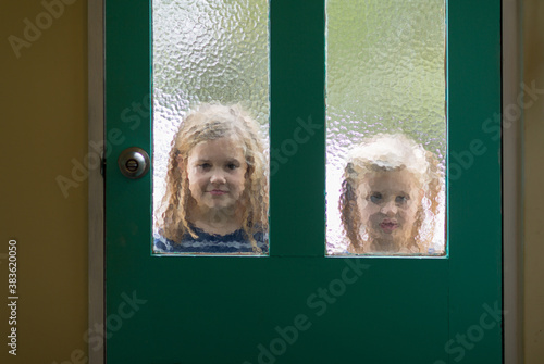 Two little girls outside looking in through door photo