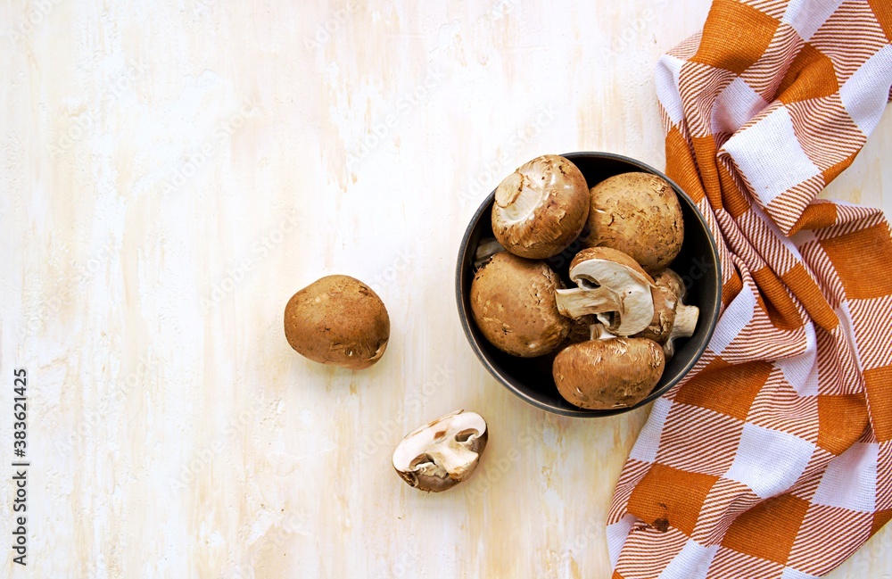 Whole and cut brown mushrooms in a clay bowl on a light concrete background. Cooking ingredients. Culinary background.