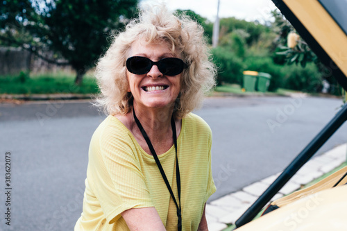 senior woman in yellow t-shirt and sunglasses packing her car in a suburban street photo