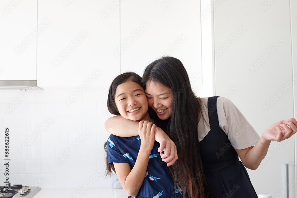 Portrait of smiling mother embracing her daughter in kitchen Portrait of smiling mother embracing her daughter in kitchen