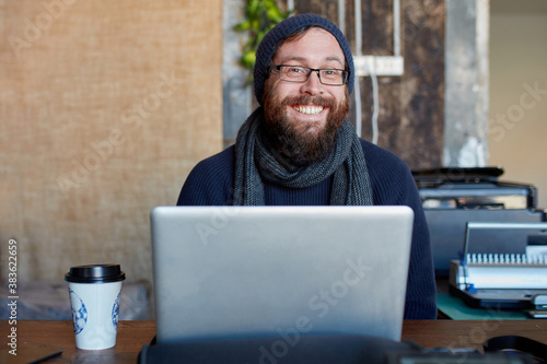 Hipster man with beard smiling at outdoor work table with a laptop photo