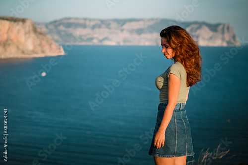 Attractive young woman posing against the blue sea and mountains at sunset. The concept of romance, travel and tourism