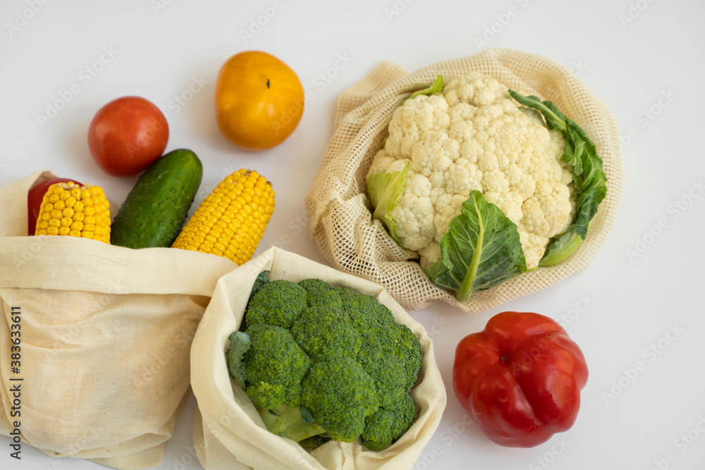 Vegetables in eco bag on white surface. Pepper, tomato, corn, cucumber, broccoli, cauliflower in reusable shopping eco friendly cotton fabric bags. Zero waste and plastic free concept. Sustainable. Vegetables in eco bag on white surface. Pepper, tomato, corn, cucumber, broccoli, cauliflower in reusable shopping eco friendly cotton fabric bags. Zero waste and plastic free concept. Sustainable.