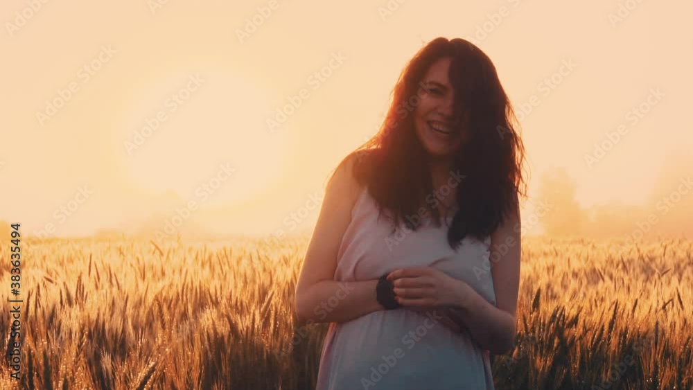 Pregnant girl laughing straightens her hair in fog on field, holding her stomach Pregnant girl laughing straightens her hair in fog on field, holding her stomach