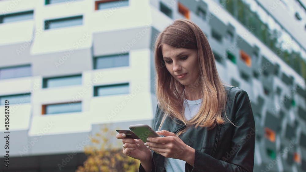 Smiling young female customer holding credit card and smartphone, on modern home background. Happy women shoppers using instant simple mobile payments while shopping online. Electronic banking service