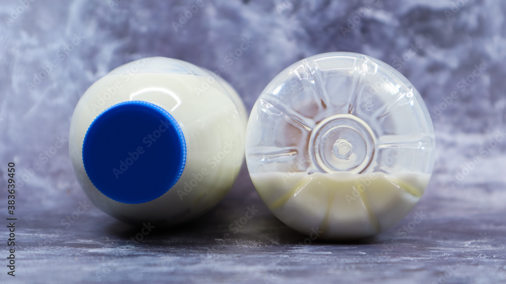 Fototapeta premium A half-empty and full plastic bottle of fresh regular milk lies on a dark gray marble or concrete backdrop. Close-up front view. World milk day concept. Nutrient fluid.