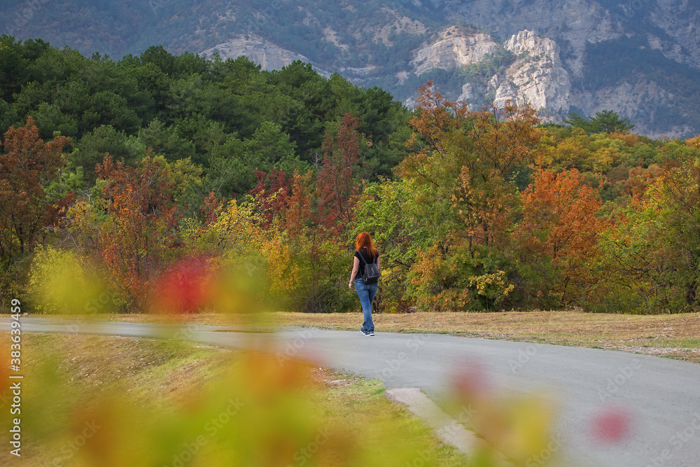Very beautiful colorful autumn landscape. Paved road in the mountains in autumn. A girl walking on an autumn road.