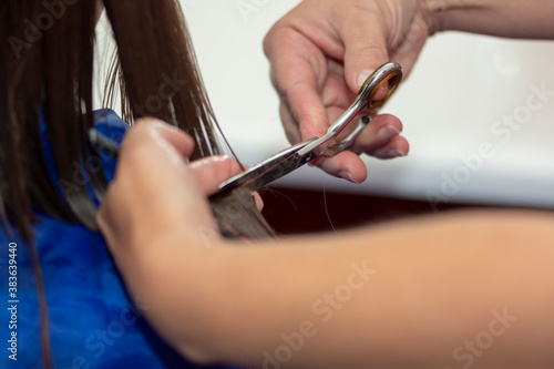 Professional female hairdresser cutting girl s brown hair in salon  closeup