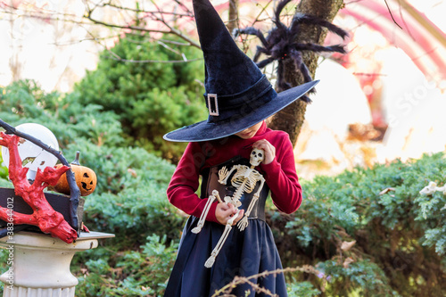Little girl in a witch costume holding a skeleton on a halloween party
