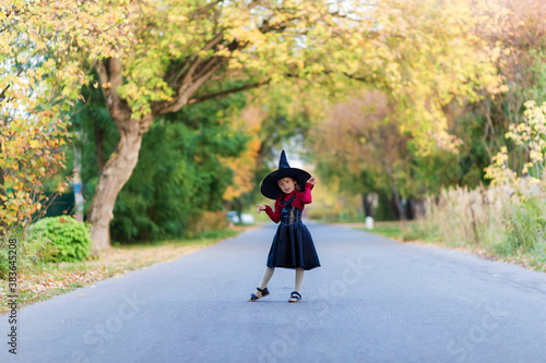 Little girl in a witch costume stands on the road on a halloween party