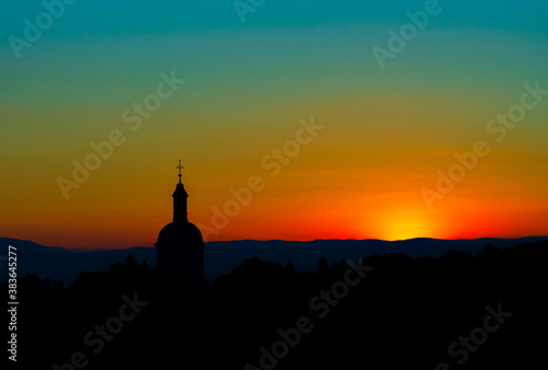 The stunning beauty and colors of the sunset overlooking the silhouettes of the Alps and the silhouette of a beautiful church